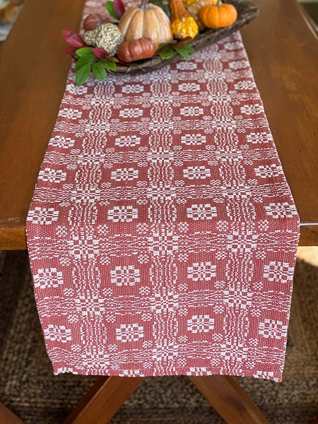 A 34-inch square table runner with a pumpkin and cream color design, laid out on a wooden table.