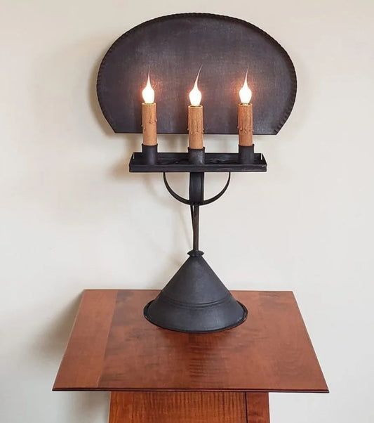 Black wall-mounted candle holder with three lit candles on a wooden surface.