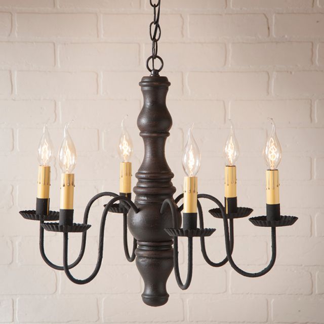 Black chandelier with six candles against a white brick wall