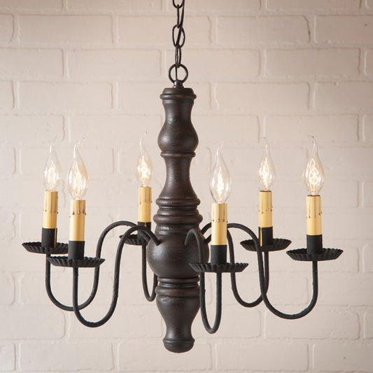Black chandelier with six candles against a white brick wall