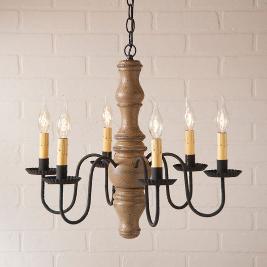 Wooden chandelier with six candle-style lights against a white brick wall.