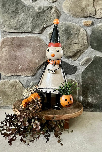 Halloween-themed decorative figure with a black hat and orange nose on a stone wall background.