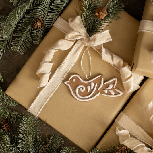 Gift wrapped in brown paper with a decorative ribbon and bird ornament, surrounded by greenery.