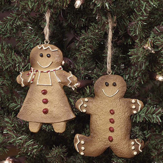 Resin gingerbread ornaments of a smiling boy and girl in traditional candy frosting and cookie decorations, hanging from twine.