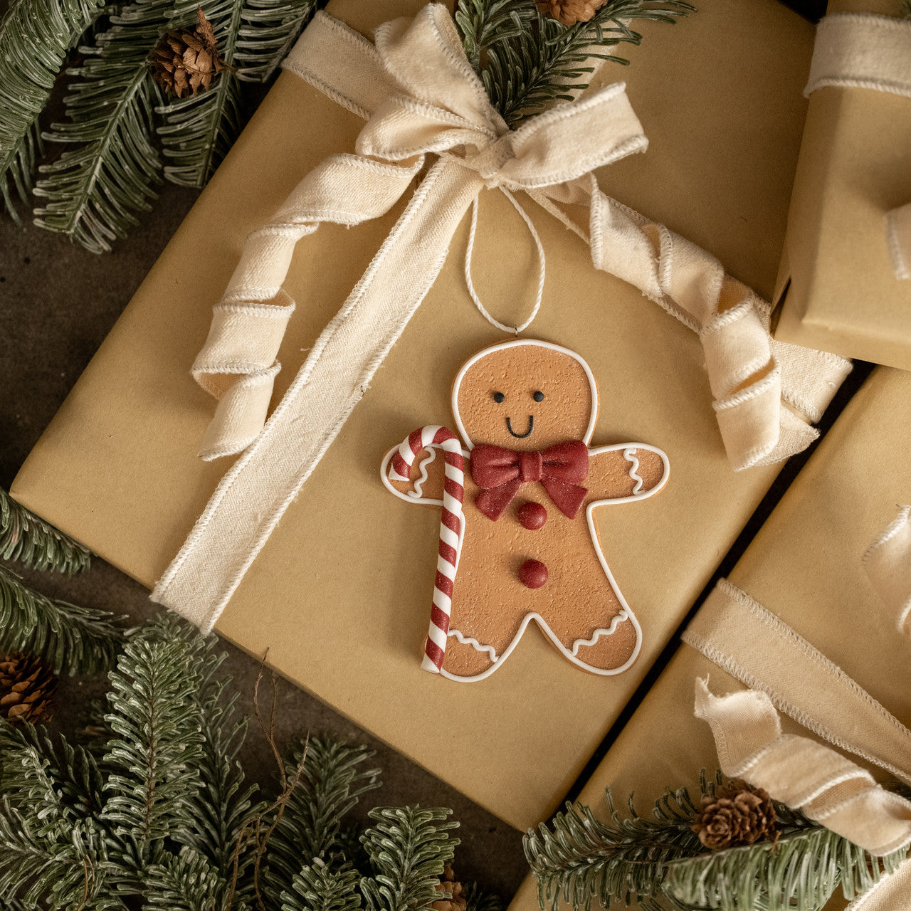Gift wrapped in brown paper with a gingerbread man ornament on top, surrounded by Christmas decorations.