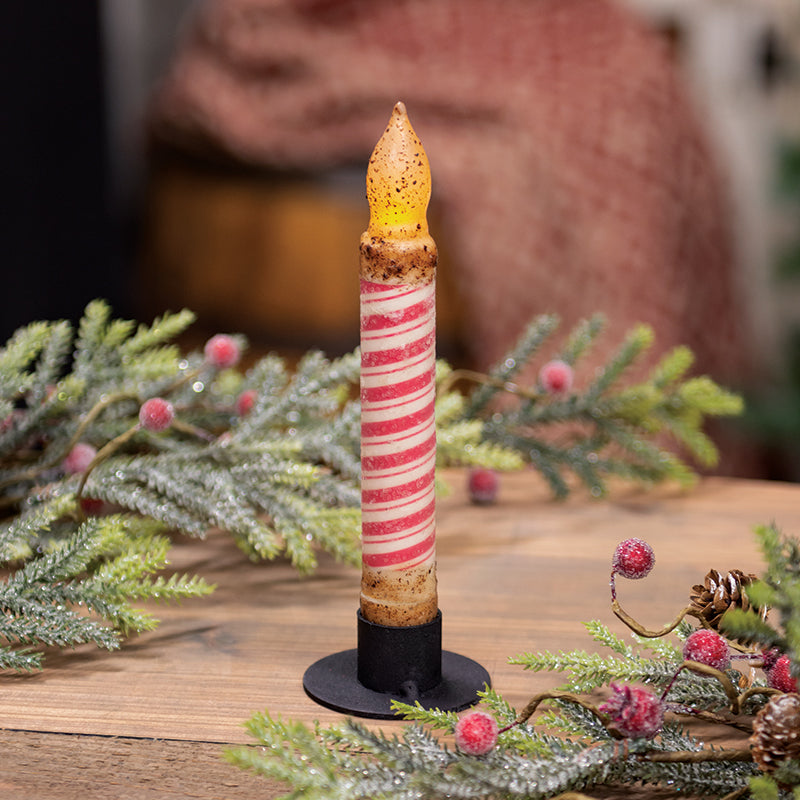 Decorative candle with striped design on a stand surrounded by greenery