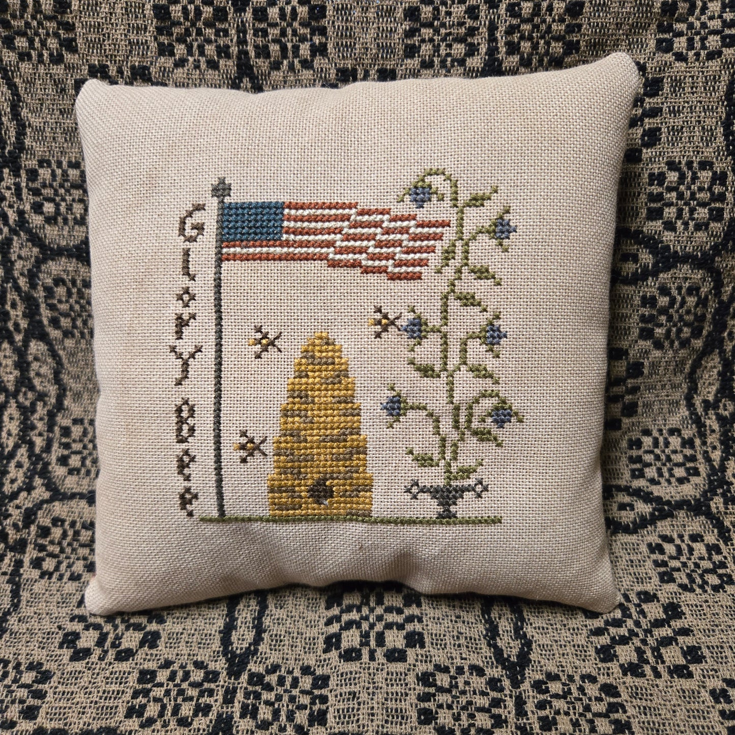 Decorative pillow with cross-stitched design on a patterned fabric background