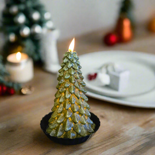 A green LED tree-shaped candle with a timer feature, displaying a lit flame at the top, placed on a black surface with a wooden background.