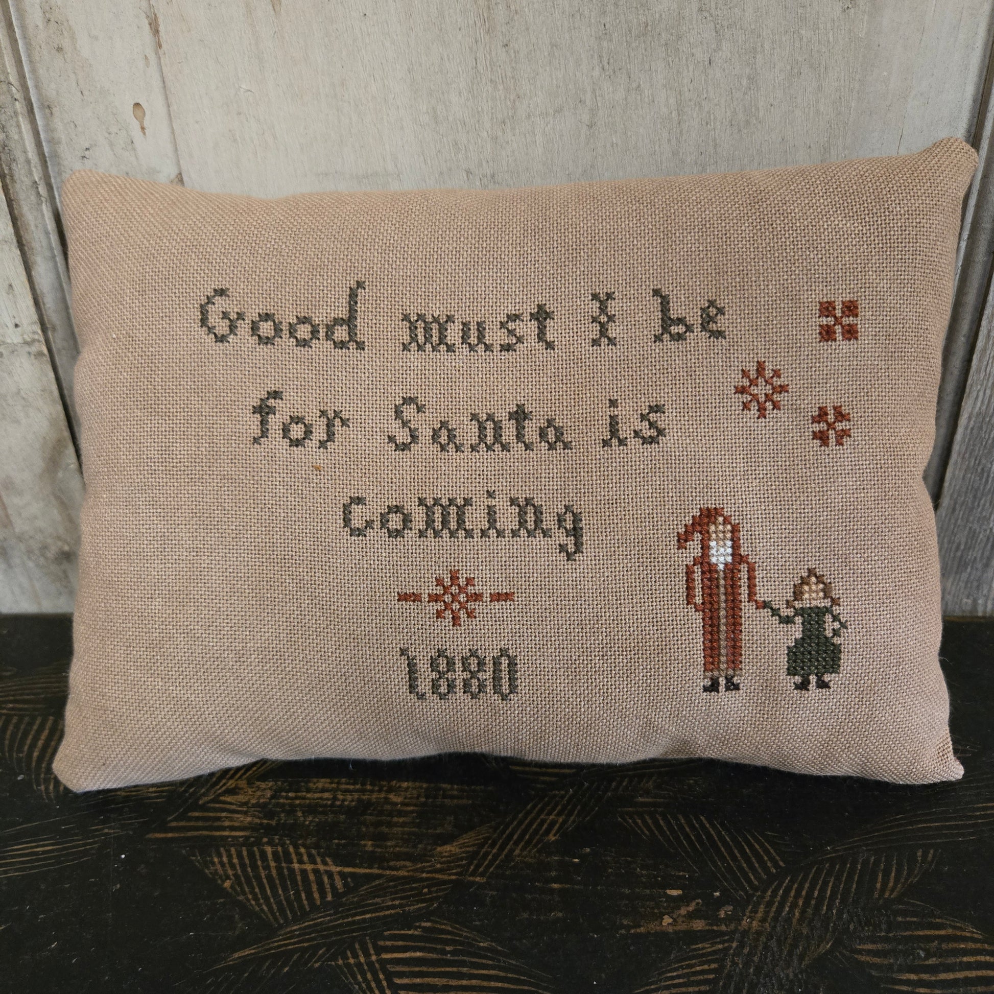 Decorative pillow with cross-stitched text and design on a wooden surface