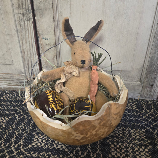 Decorative Easter basket with a plush bunny, eggs, and carrots on a textured surface.