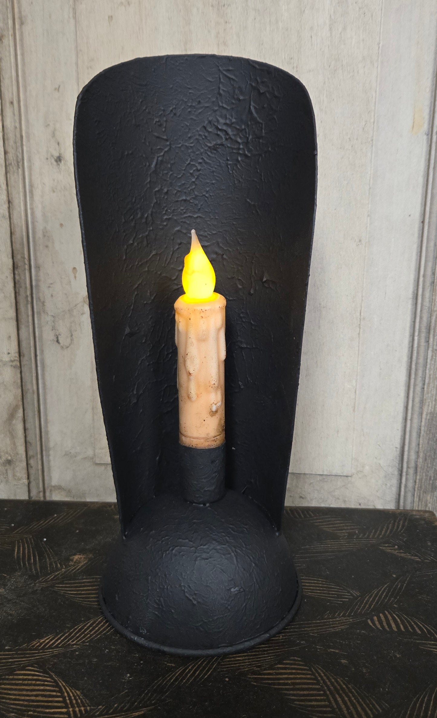 Black decorative item with a lit candle inside on a textured surface.