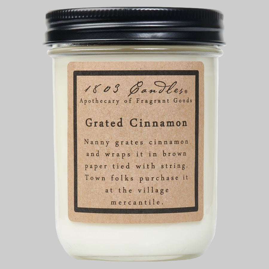 A jar candle labeled '1803 Candles, Grated Cinnamon' with a brown paper lid and a black label on a clear jar.