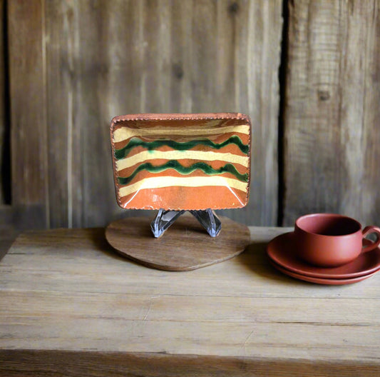 Ceramic dish with wavy pattern on a stand, next to a cup and saucer on a wooden surface.
