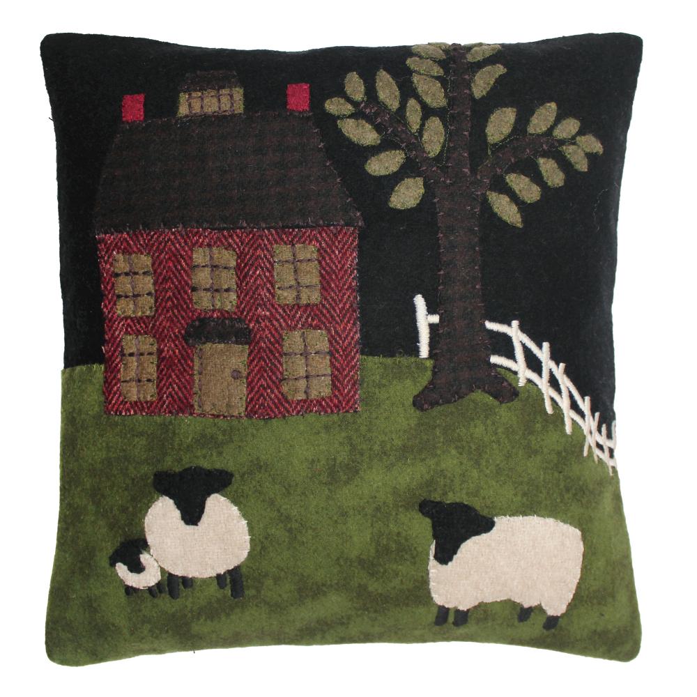 Decorative pillow with a house, tree, and sheep design on a black background