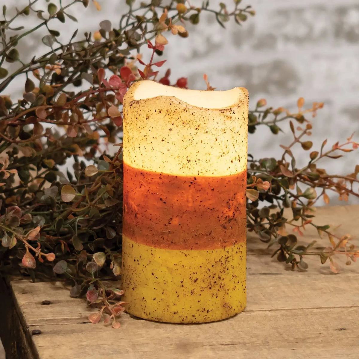 Decorative candle with a layered design on a wooden surface with plants in the background