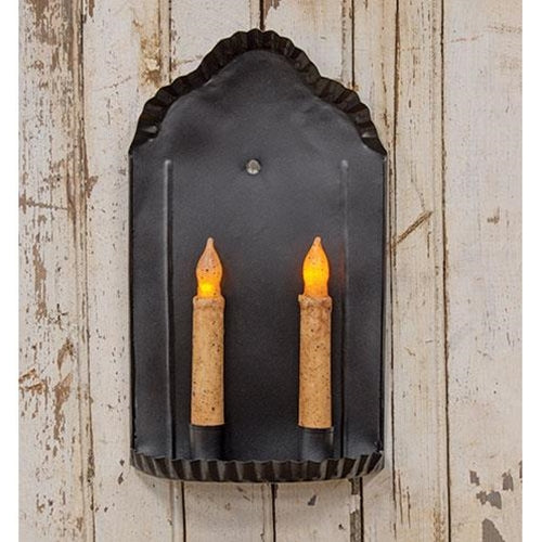 A black metal sconce with two faux taper candles displayed against a wooden background.