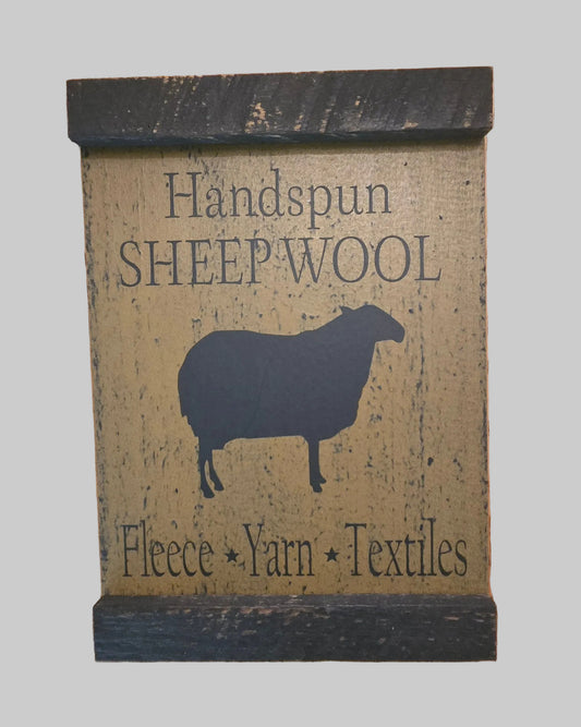 Decorative sign with 'Handspun Sheep Wool' text and a sheep silhouette on a wooden background.