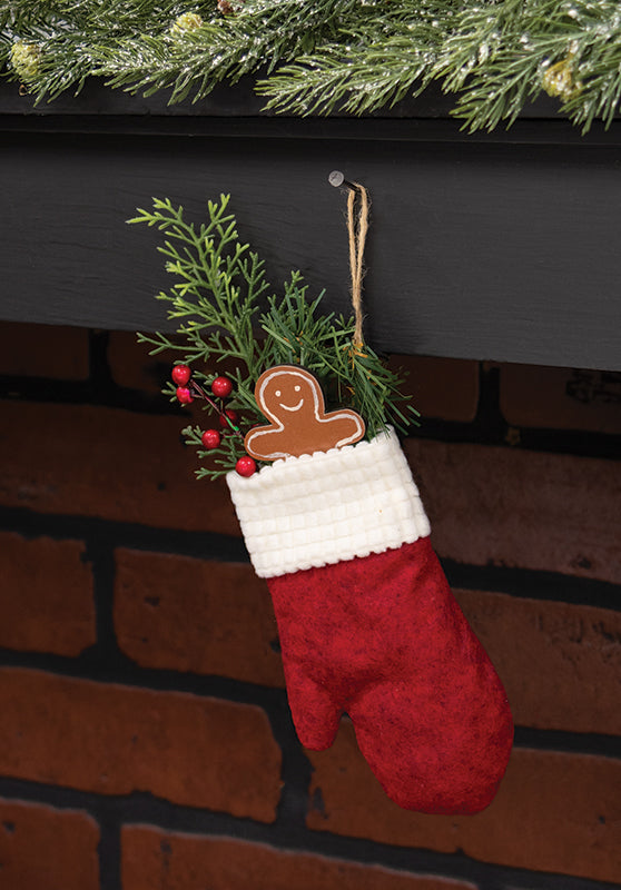 Red Christmas stocking with a gingerbread man ornament hanging on a fireplace.