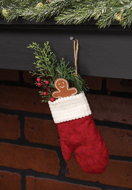 Red Christmas stocking with a gingerbread man ornament hanging on a fireplace.