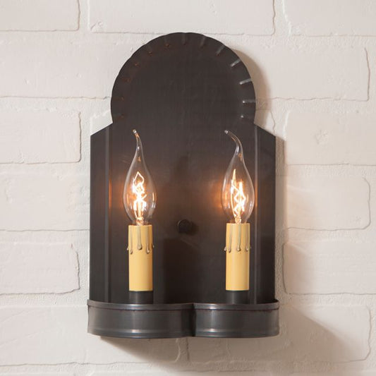 Wall-mounted sconce with two lit light bulbs against a white brick wall.