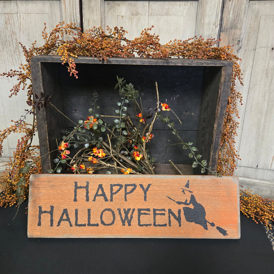 Decorative Halloween sign with 'Happy Halloween' text and a witch on a broomstick, placed against a wooden wall.