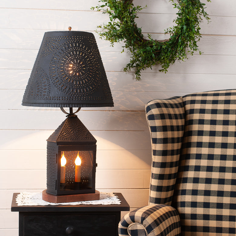 Decorative lamp with black shade on a side table next to a plaid chair.