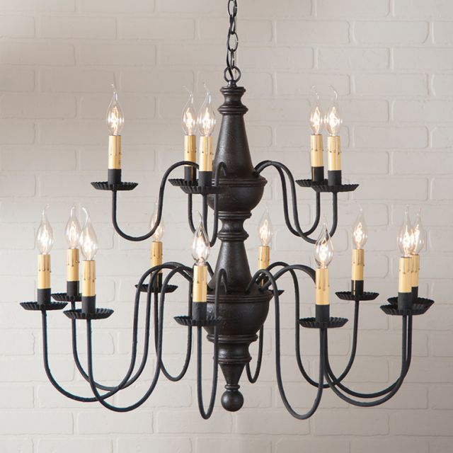 Black chandelier with multiple candle-style lights against a light brick wall.