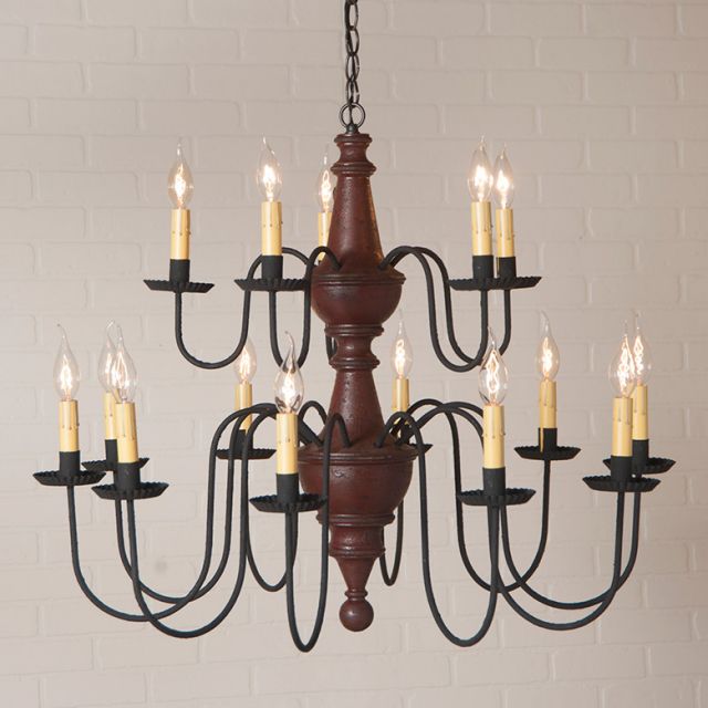 Vintage-style chandelier with wooden center and black metal arms against a light brick wall.