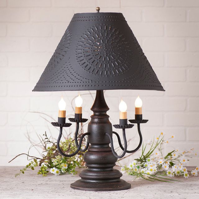 Decorative table lamp with a black perforated shade on a white brick wall background.