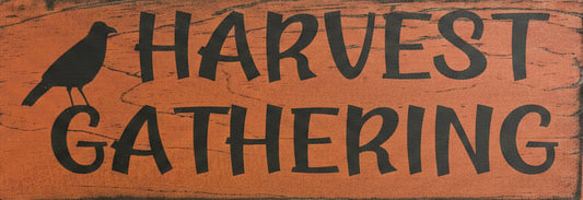 A rustic wooden sign with a distressed orange-brown background and black painted text reading 'HARVEST GATHERING,' plus a black bird silhouette on the left.