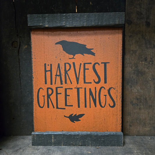 Wooden sign with 'Harvest Greetings' text and bird silhouette on a dark background