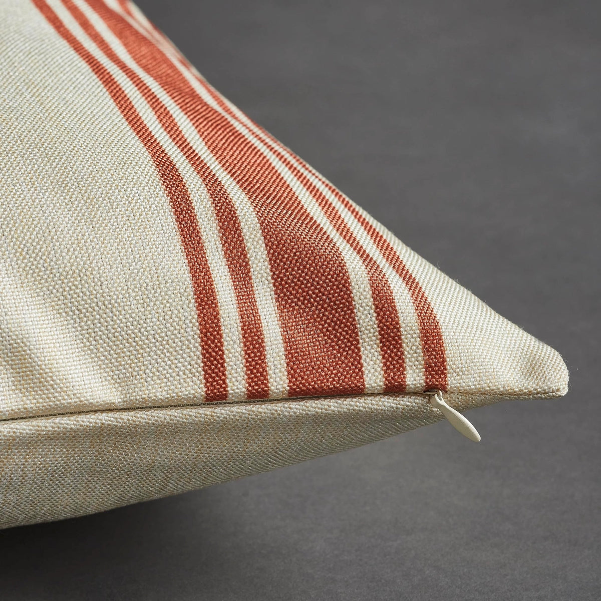 Close-up of cream woven pillow cover fabric with rust-colored stripes and a concealed zipper along the edge.