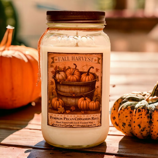 A white Harvest Mason Jar Candle with a fall-themed label, containing scented wax and set on a table with pumpkins in the background.