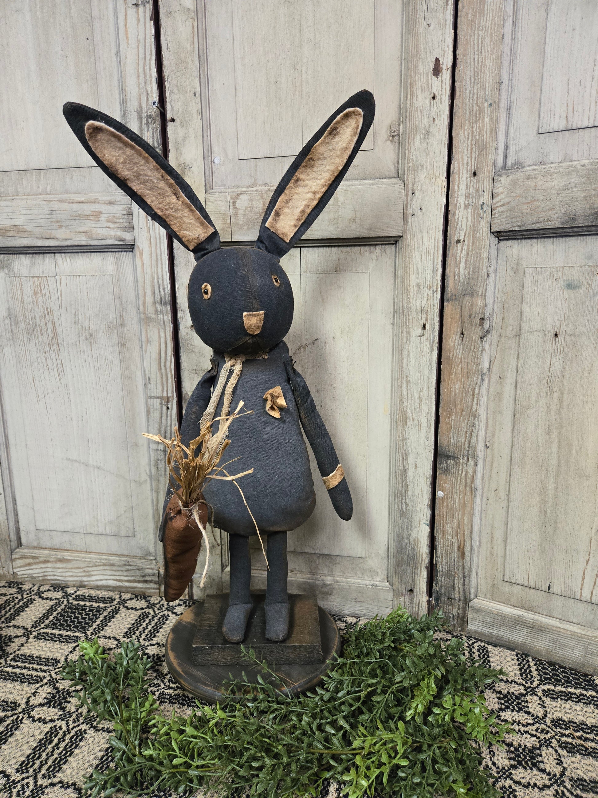 A figurine of a black bunny with a carrot, standing on a base, positioned against a wooden backdrop.