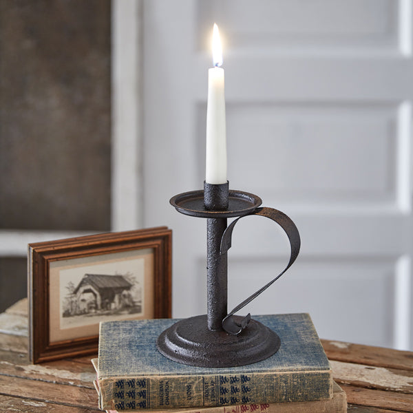 Black candlestick holding a white, burning candle sitting on an antique book with a photo next to it