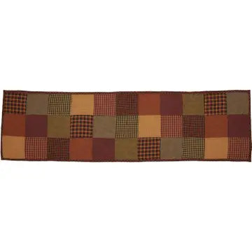 A rectangular patchwork table runner featuring a rustic grid pattern of squares in earthy tones of brown, rust red, tan, and olive green, including plaid and checkered designs, shown against a plain white background.