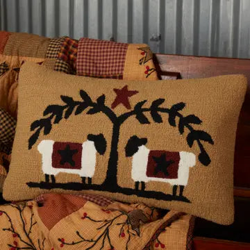 A rustic woven throw pillow with a burlap-textured tan background, featuring a black tree with two white sheep under a red star.