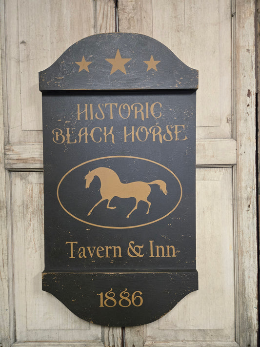 Decorative sign for Historic Black Horse Tavern & Inn with gold text and horse silhouette on a wooden background.