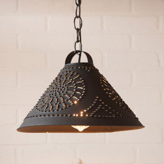 Hanging pendant light in black with chisel piercing pattern on white brick background.