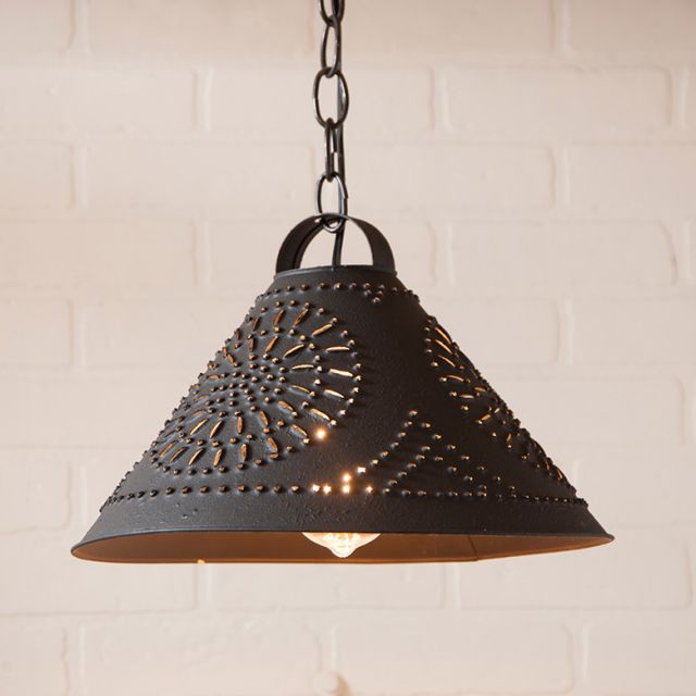 Black pendant light with decorative pattern against a white brick wall