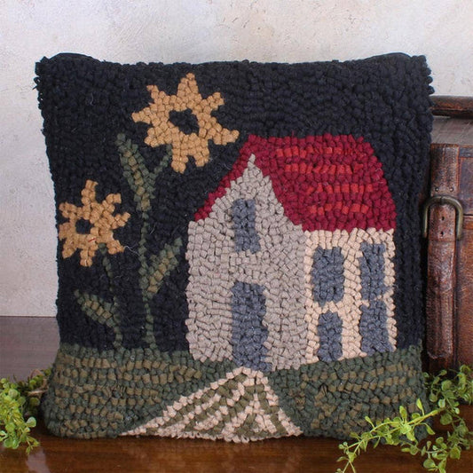 Decorative pillow with a house and flower design on a wooden surface.