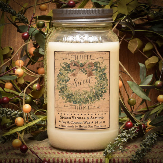 A mason jar candle with a label that reads 'HOME Spice Vanilla Almond', surrounded by greenery and berries.