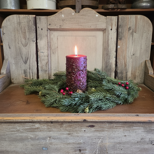 Purple candle in a decorative wreath on a wooden surface with a rustic background