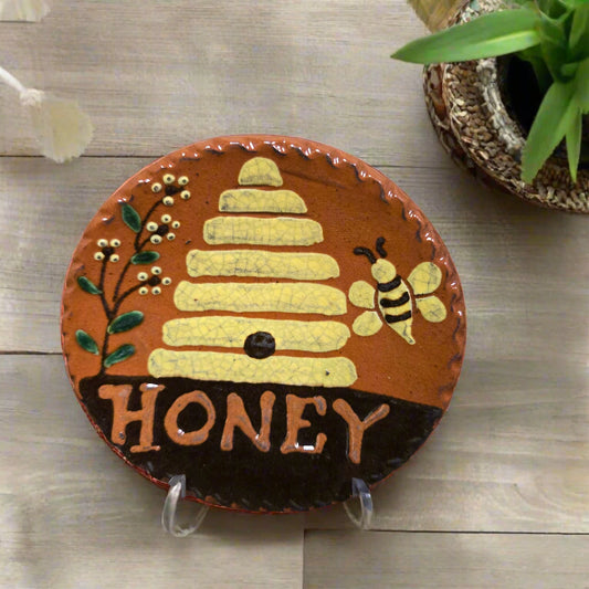 Redware plate with a beehive and bee design, labeled 'HONEY', on a wooden surface.