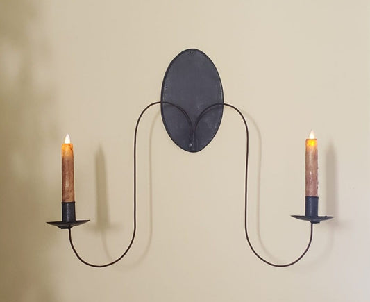 A wall-mounted tin sconce with a reflective metal backplate and two extended arms, each holding a candle.