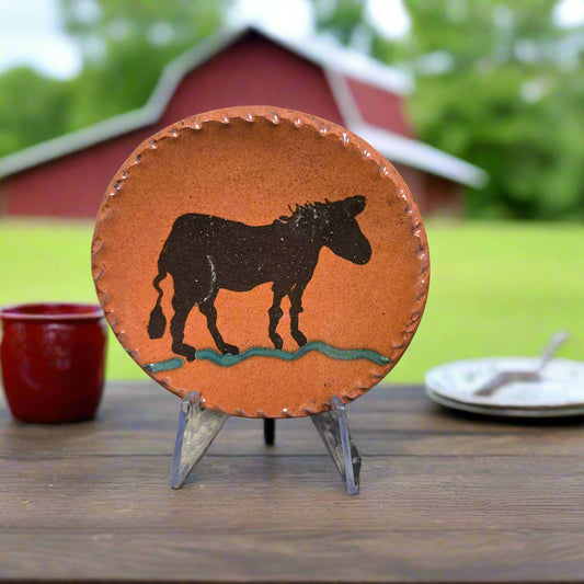 Decorative plate with a horse design on an easel in front of a red barn.