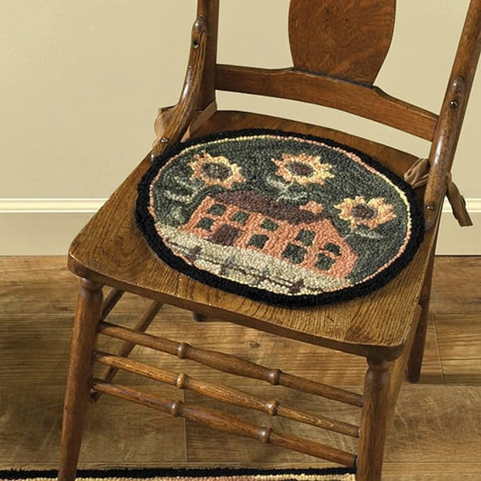 A hooked chair pad with a house and sunflower design, placed on a wooden chair.