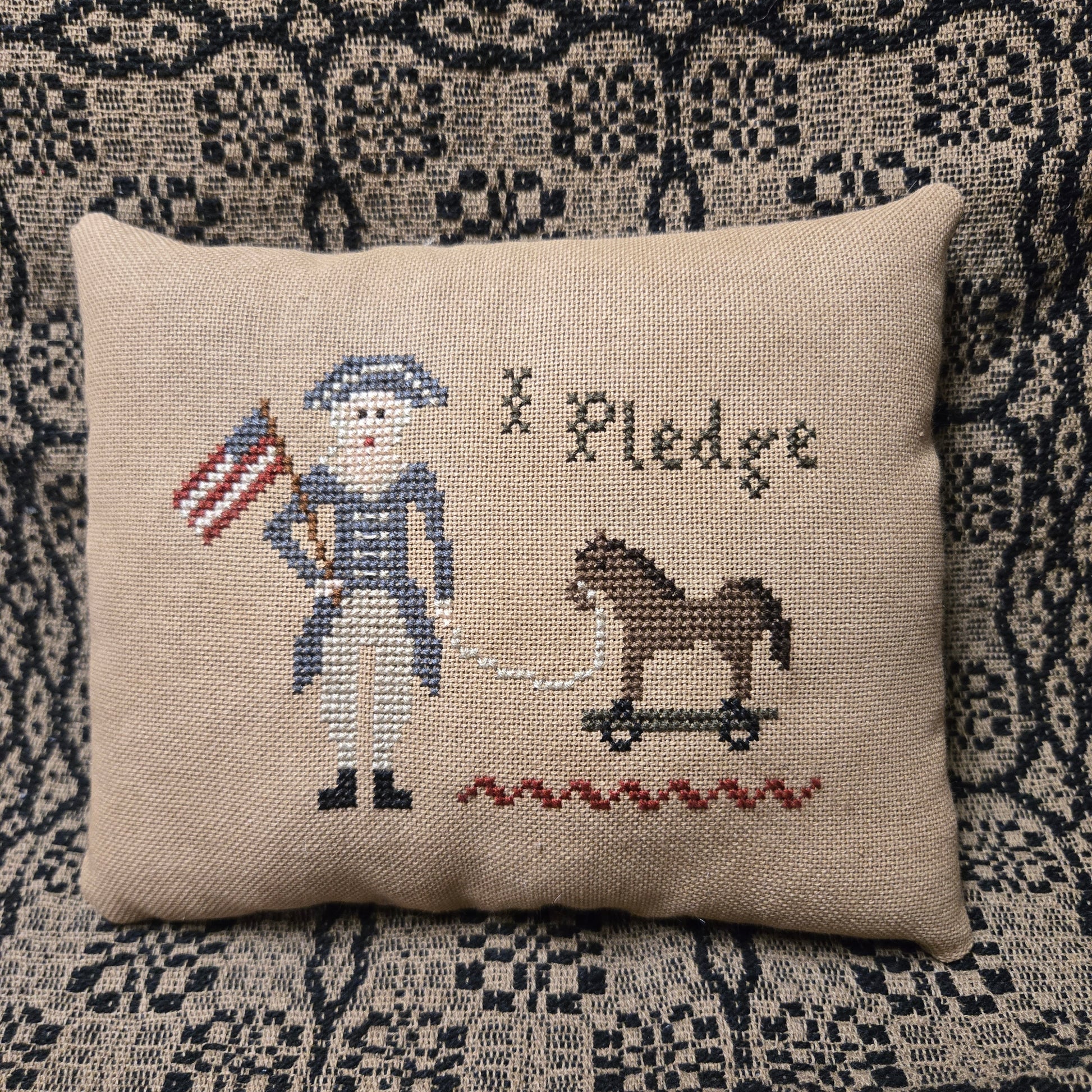 Decorative pillow with cross-stitched design of a soldier and flag on a textured surface