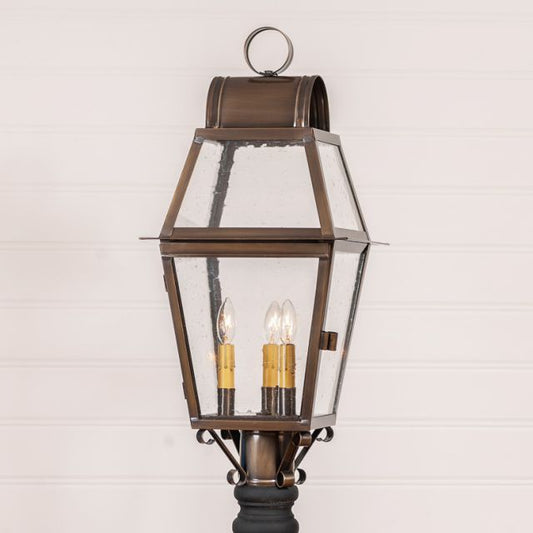 A solid weathered brass outdoor post light with three lights, historic glass, and a blackened solder finish.