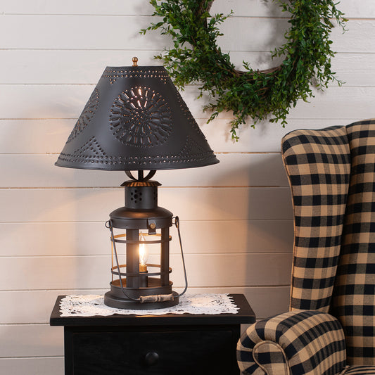 Decorative table lamp with intricate design on a small table next to a plaid chair.